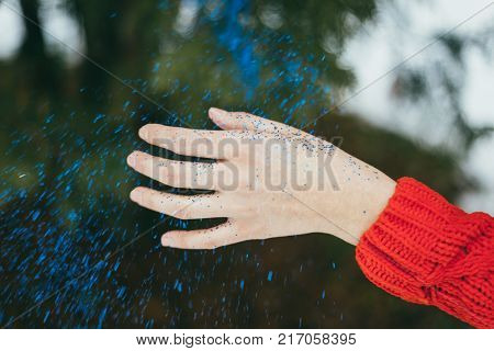 Young beautiful girl blowing on hands with blue glitters on green background.