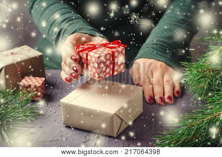 Female hands wrapping and present Christmas gifts on dark background with showflakes. Horizontal, toned