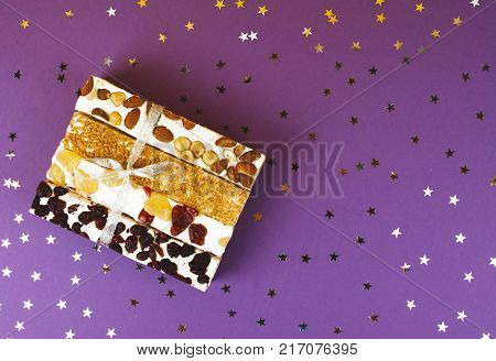 Traditional italian festive torrone or nougat with nuts on lilac background.