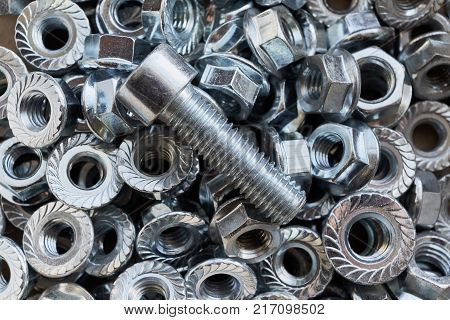 Shiny metal bolt lying on a pile of scattered nuts. Abstract background for industry from the new shiny nuts. Bolt and nuts for fixing. Chaos and confusion from the nuts.