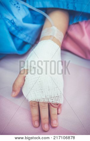 Close up of saline intravenous (iv) drip in a child's patient hand. Illness child admitted in hospital. Health care stories. Vintage film filter effect.