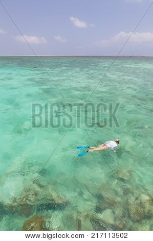 Woman snorkeling in clear shallow sea of tropical lagoon with turquoise blue water and coral reef, near exotic island. Mnemba island, Zanzibar, Tanzania.