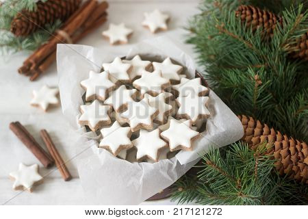 Cookies cinnamon star in a tin box on a background of cinnamon sticks, fir branches and cones. Selective focus.