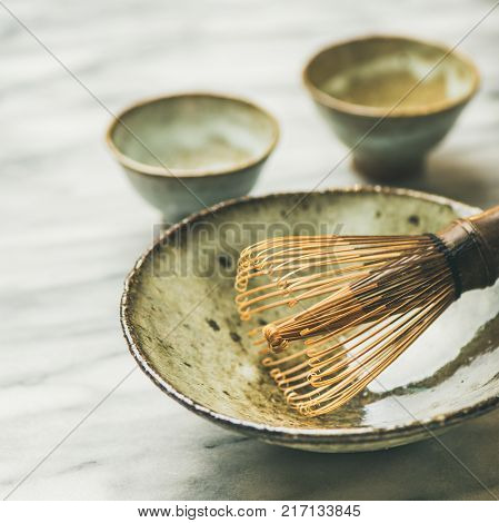 Japanese tools for brewing matcha tea. Matcha powder in tin can, Chasen bamboo whisk, Chawan bowl, cups for ceremony, grey marble background, selective focus