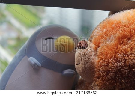 Bear and penguin toy sitting by the window in shadows