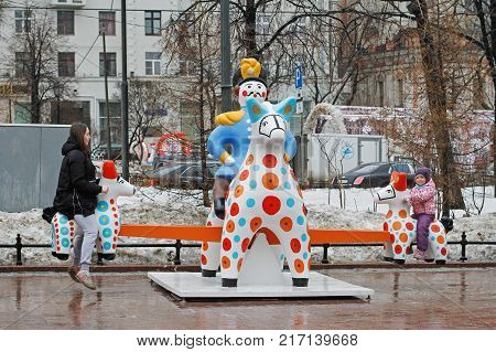 Moscow Russia - February 21 2017: Mother with daughter playing seesaw in Novopushkinsky square in Moscow. Traditional Dymkovo toy man on horse as art object and swing at Russian national festival 