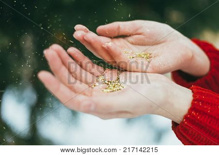 Young curly girl in crystal sunglasses blowing on hands with golden glitters on blue background.
