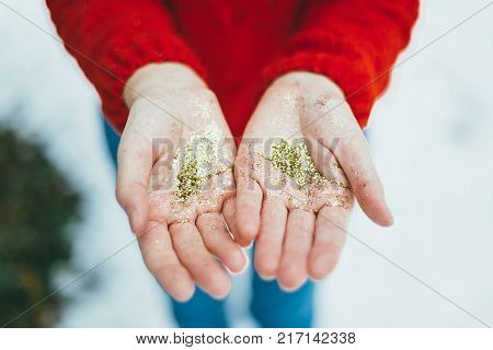 Young curly girl in crystal sunglasses blowing on hands with golden glitters on blue background.