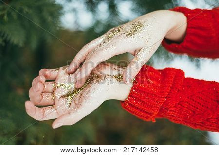 Young curly girl in crystal sunglasses blowing on hands with golden glitters on blue background.