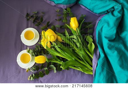 Yellow tulips and two cups of tea in bed, morning