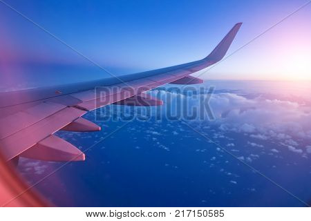 View from passenger's seat in airplane flying above clouds in dramatic sunset light. High resolution of image. Fast Travel and transportation concept