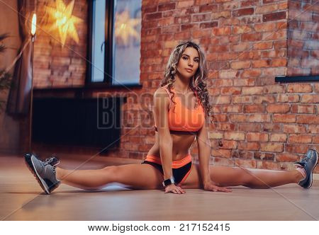 Attractive blond fitness female stretching in a split at home.