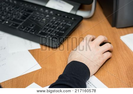 Top view of man's hand on computer mouse with black keyboard and paper on desk