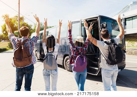 Four tourists raised their hands up and pose for a photo. They raised their hands up. Against the background is a modern black bus on which they will travel.