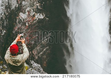 Traveling Man taking photo of Vettisfossen waterfall using smartphone on cliff adventure lifestyle concept extreme vacations outdoor wanderlust
