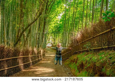 Happy tourist woman jumping in bamboo forest at Sagano in Arashiyama, kyoto, japan. Travel asia concept. Freedom and enjoying concept. Kyoto's popular landmark and touristic destination.