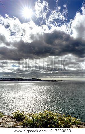 View of the entrance of the bay of La Coruna with the silhouette of the City of La Coruna Galicia. Dramatic sky with dark clouds and sun facing