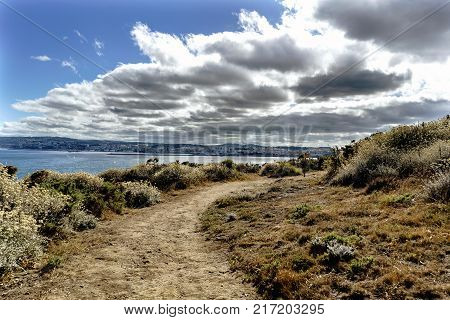 Road on the cliffs on the coast of La Coruna Bay (Galicia) on the Spanish Atlantic coast with the city of La Coruna in the background. Blue sky with some clouds and calm sea