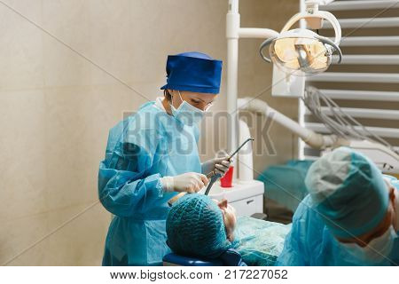 Male Old Professional Dentist Surgeon In Uniform And Female Assistant Helps To Performing Operation