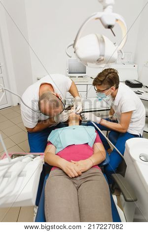 Process of preparing and installing dental ceramic crown. Male professional dentist and female assistant helps to treat the teeth of woman patient in clinic light office with modern tools equipment