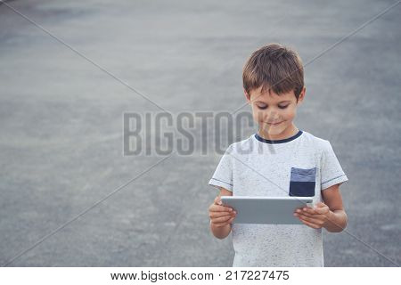Happy kid playing with tablet computer outdoors