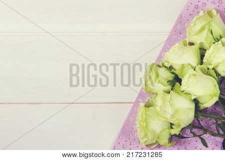 White green roses on rustic wood background with lilac paper