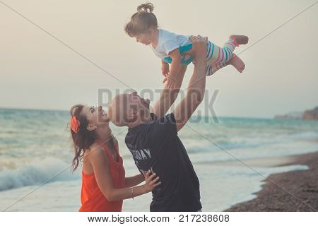 Family Together Enjoying Summer Vacation Time On Sandy Beach On Amazing Scene Of Sea Cliff And Sky W