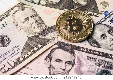 The golden bitcoin lies on the background of dollar bills. Close-up.