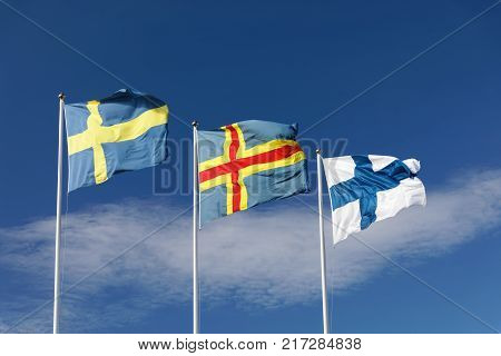 Flags from Sweden Aland and Finland on flag poles blue sky and white cloudes