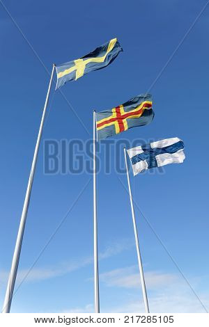 Flags from Sweden Aland and Finland on flag poles blue sky and white cloudes