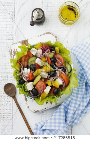 Greek salad in a ceramic plate on a white wooden background. Traditional Greek dish. Selective focus.Top view.