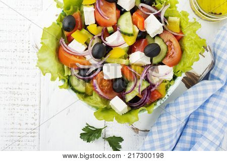 Greek salad in a ceramic plate on a white wooden background. Traditional Greek dish. Selective focus.Top view.