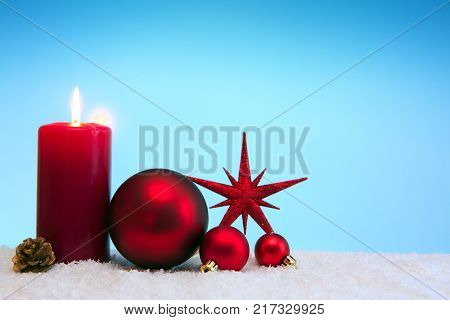 Avent candle and christmas decoration isolated on blue background. Christmas background with snow, candle and red star.