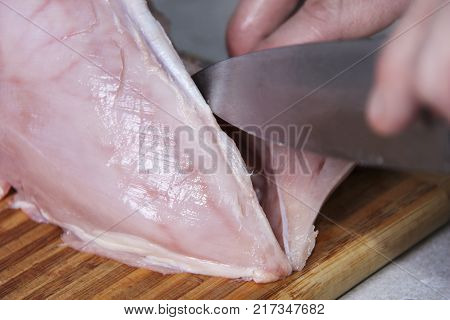 Man's hand cutting raw chicken breast. Selective focus