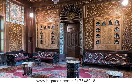 Cairo Egypt - December 2 2017: Manial Palace of Prince Mohammed Ali. Guests Hall with wooden ornate ceiling wooden ornate door lanterns colorful ornate couches tea tables and ornate carpet