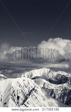 Winter snowy sunlit mountains and sky with clouds. Caucasus Mountains Georgia region Gudauri. Black and white view from ski resort.