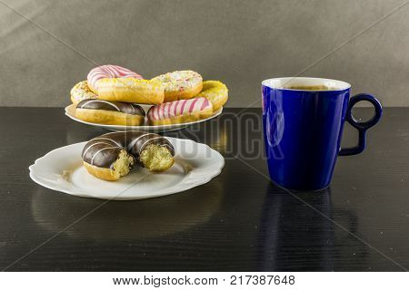 Break for something sweet. Bitten chocolate doughnut and a mug of coffee on the table.