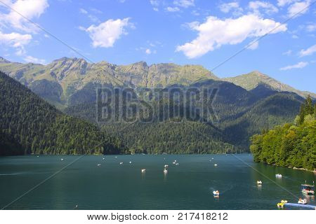 Beautiful panorama of natural mountain landscape with clouds. Pleasure boats on the water. Blue Lake Ritsa among mountains of the Caucasus, Abkhazia. Ritz Park