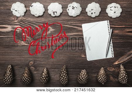 Brown wood background. Gold cones and sweet biscuits arranged diametrically opposed. Letter and space for a greeting message. Top View. With Christmas.