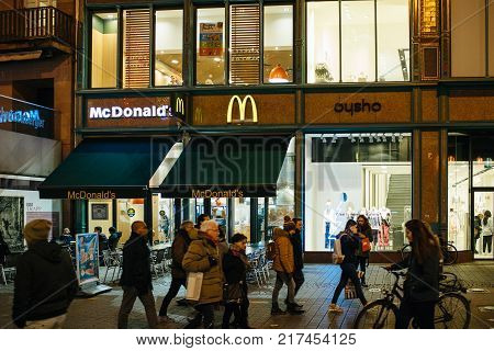 STRASBOURG FRANCE - NOV 29 2017: McDonald's restaurant in cetntral Strasbourg at night with pedestrians walking on busy pedestrian street