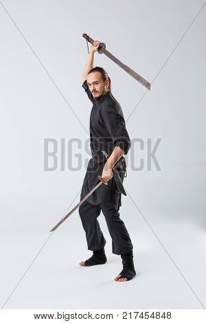A black ninja man holding two swords in his hands at the top swings and down directed down on a gray background