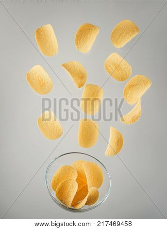 Tasty potato chips falling to bowl on blue background