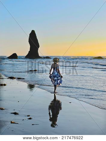 Woman on sandy beach watching sunset over the sea. Sea stacks on Shi Shi Beach.