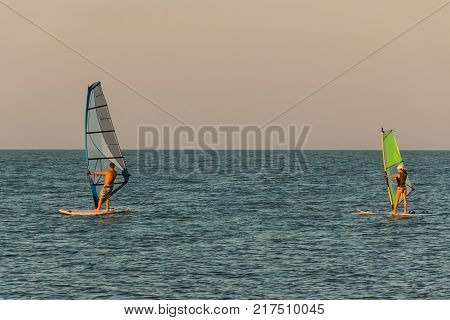 A man and a woman swim on the sailboards while windsurfing.