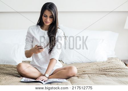 Beautiful woman in a shirt talking on the phone and reading the morning paper on the luxorious bedroom bed