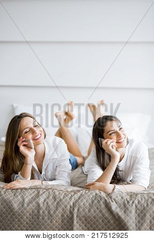 Two beautiful girls talking on the phone and smiling while lying on a luxorious  bed