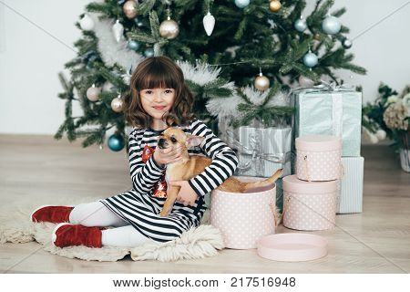 The girl sits at the tree and looks at the gifts. New Year holidays. The time to realize dreams. A gift in the box. New Year's Symbol