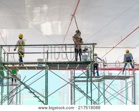 Worker man painting a gypsum plaster ceiling with paint roller on the scaffold