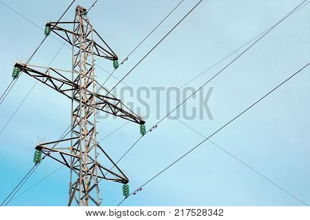 The support of the overhead power line is 35 kilovolts. Electricity. The support is silvery. Insulators are green. The wires diverge in different directions. Blue sky background.