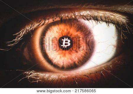 An enlarged image of eye with a brown iris, eyelashes and sclera. Bitcoin symbol inside the pupil. the shot is made by a slit lamp with integrated camera.